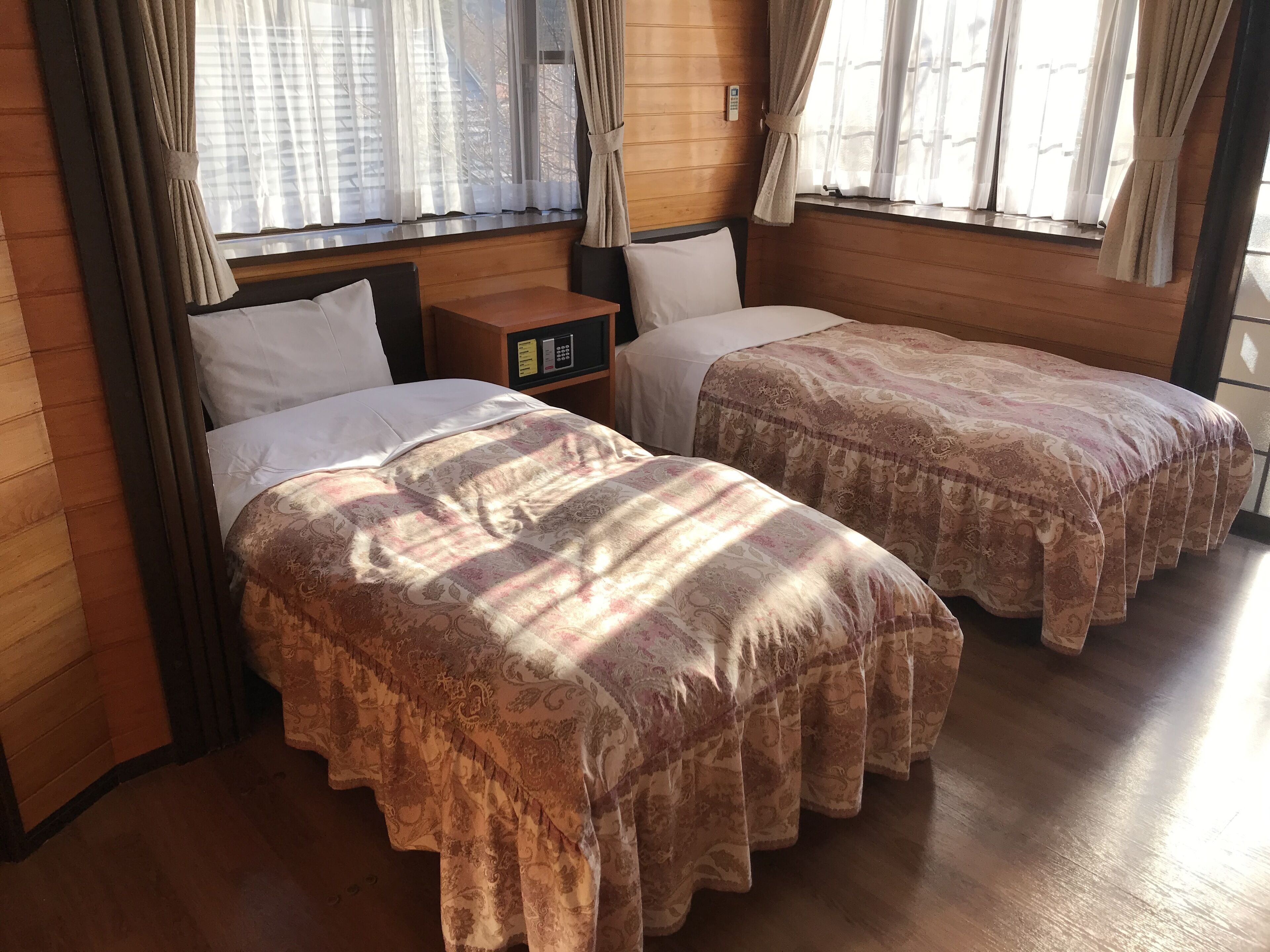 Une chambre avec deux lits, des murs en bois et une petite table de chevet dotée d’un panneau de commande.