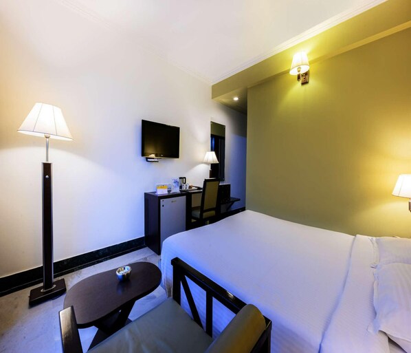 A hotel room with a bed, a desk, a chair, a table, and a TV.