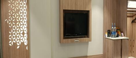 A modern bathroom with a wooden vanity, a mounted TV, and a shelf with toiletries.