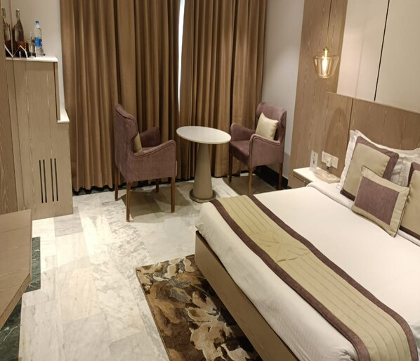 A hotel room with a bed, two chairs, a small table, and a minibar.