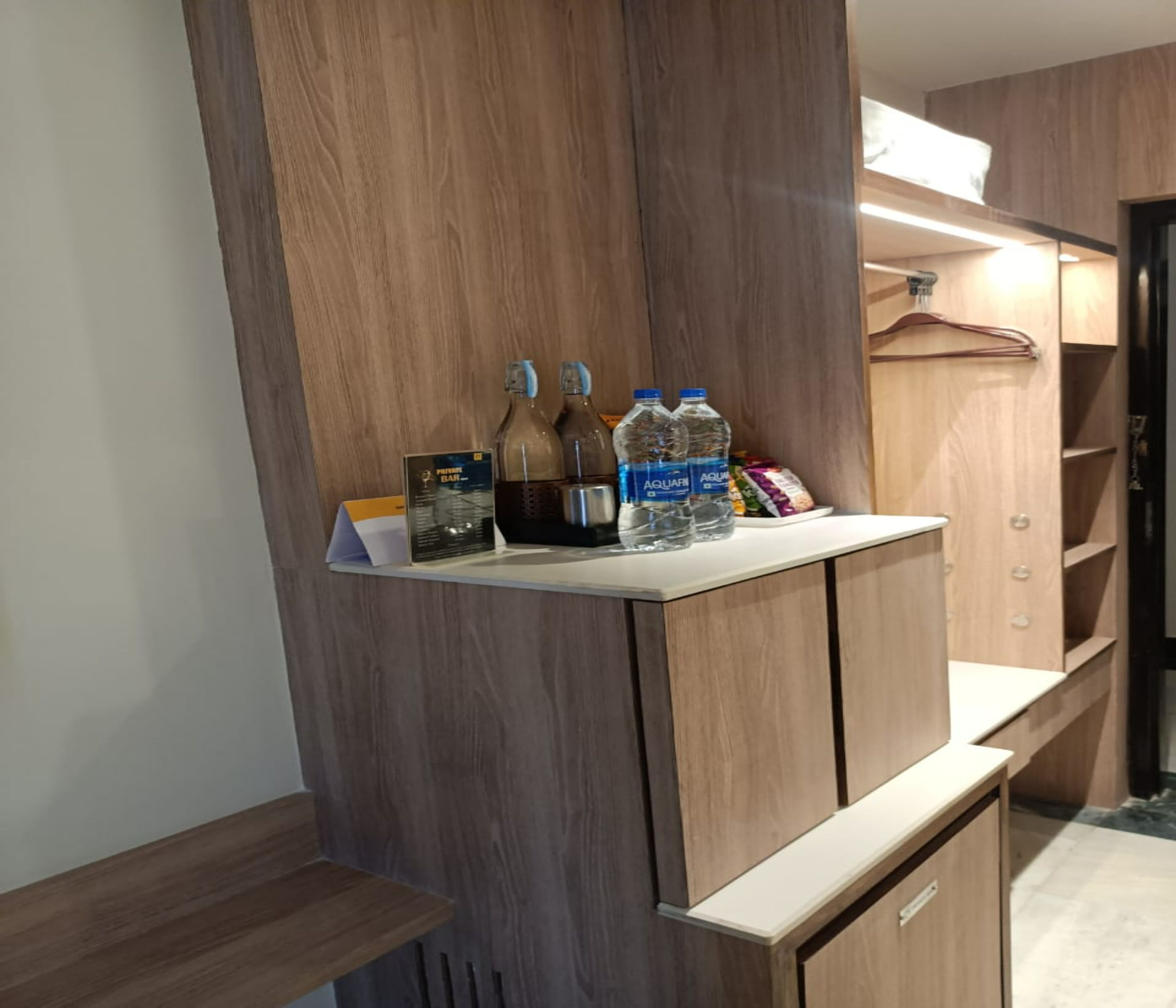 A wooden vanity with a mirror, two bottles of water, a bottle of juice, and a small bar area with a menu.