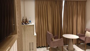 Et moderne hotelværelse med et fladskærms-tv, minibar, et rundt bord med to stole og store gardiner.