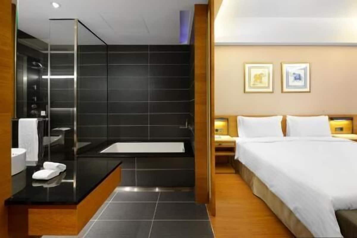 A modern hotel room with a large bed, a separate bathroom with a bathtub, and a small bedside table.