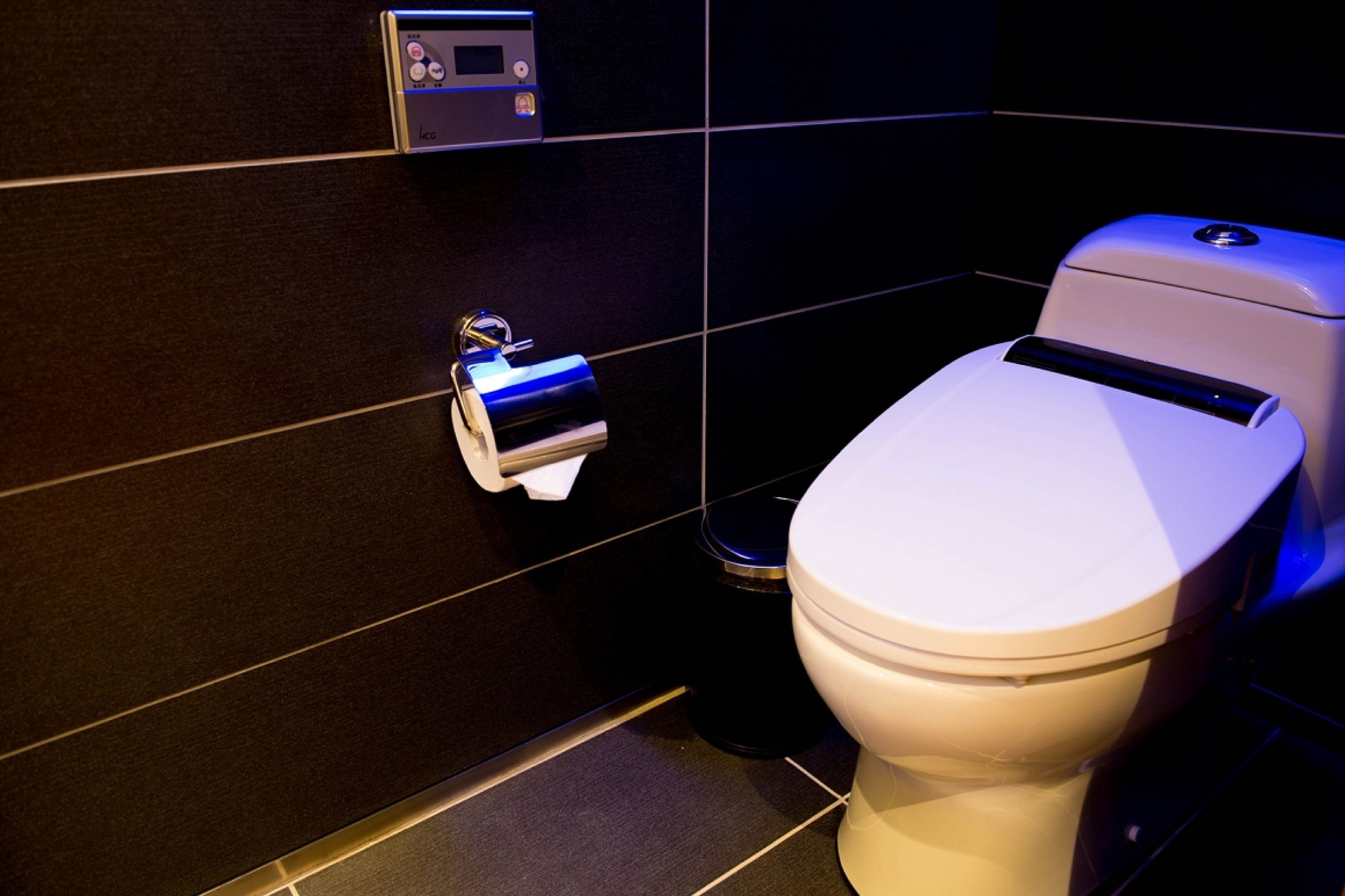 A modern bathroom with a toilet, a paper towel dispenser, and a trash bin.
