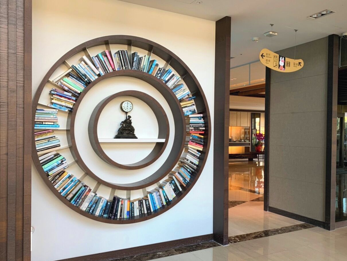 A circular bookshelf with books arranged in concentric circles, a clock in the center, and a directional sign on the wall.