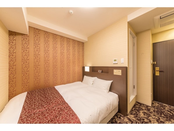 Quarto de hotel com uma cama grande, papel de parede estampado, cabeceira de madeira, uma porta e piso coberto de carpete.
