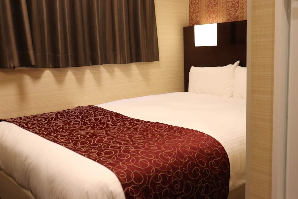 Cama bem arrumada com colcha estampada, cabeceira com interruptor de luz e janela com vista para o exterior.