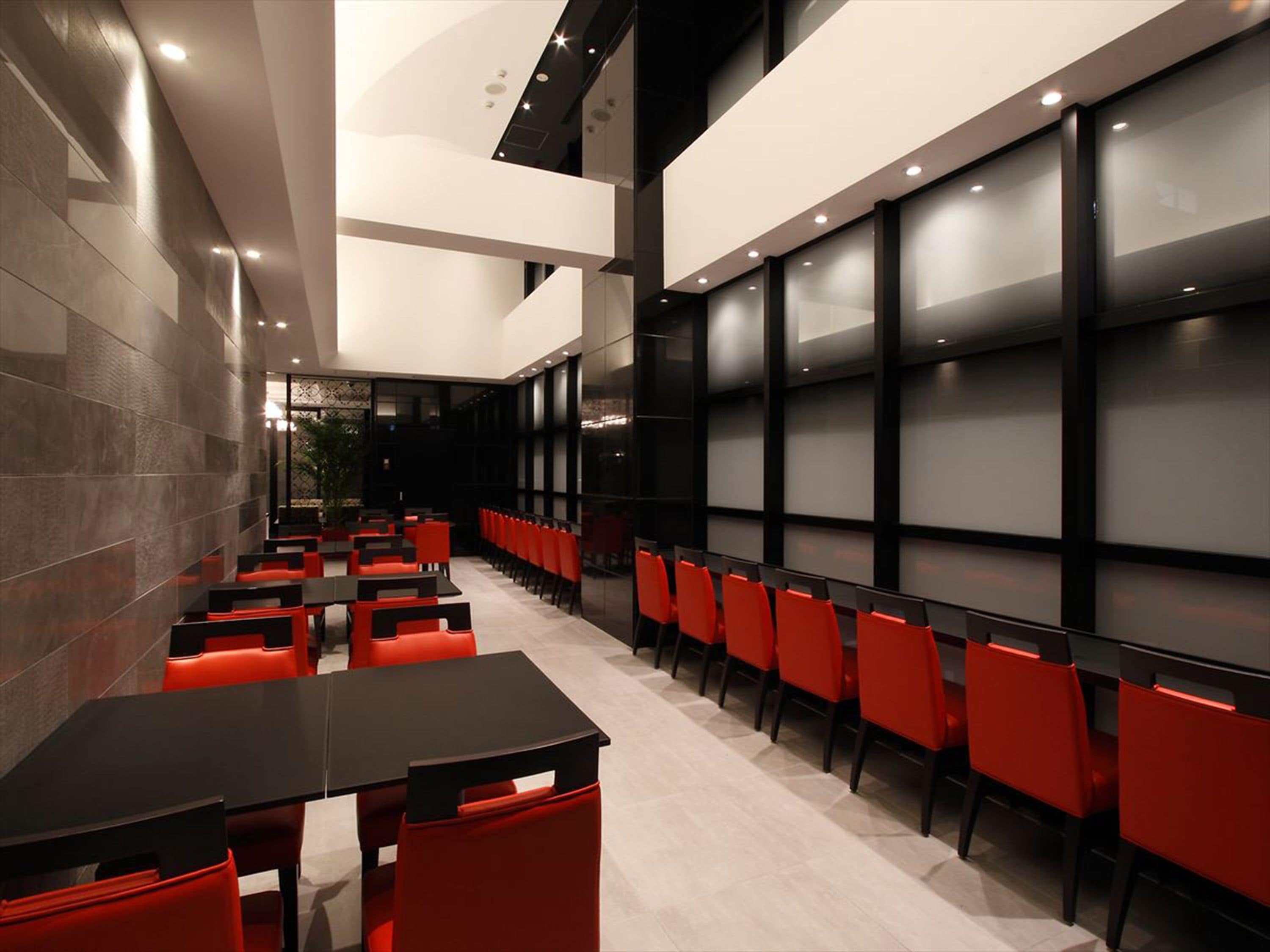 Un restaurant moderne avec des chaises rouges et des tables noires, doté d’un plafond haut et de grandes fenêtres.