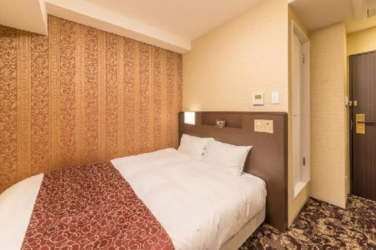 Quarto de hotel com cama, cabeceira, porta e papel de parede estampado.