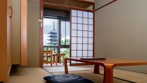 A traditional Japanese room with tatami flooring, a low table, a cushion, and a sliding door leading to a balcony with a pagoda view. - NARA Visitor Center & Inn (Nara)