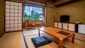 A traditional Japanese room with tatami flooring, a low table, a television, and a sliding door leading to a balcony with a view of a pagoda. - NARA Visitor Center & Inn (Nara)