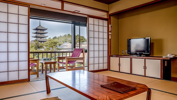 A traditional Japanese room with tatami flooring, a sliding shoji screen, a wooden table, a television, and a view of a pagoda through the window. - NARA Visitor Center & Inn (Nara)