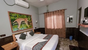 A hotel room with a bed, a nightstand, a mirror, a window with curtains, and a wall-mounted air conditioner. - Gorkha Hamlet Resort (Sauraha)