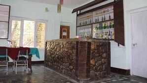 A room with a stone bar, a table with chairs, and a shelf with bottles. - Gorkha Hamlet Resort (Sauraha)