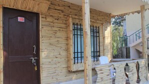A building with a dark brown door, a checkered floor, and a bamboo exterior. - Gorkha Hamlet Resort (Sauraha)