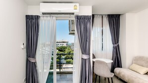 Ein modernes Zimmer mit Schiebeglasfenster zum Balkon, einer Couch, einem kleinen Tisch und einer Klimaanlage.