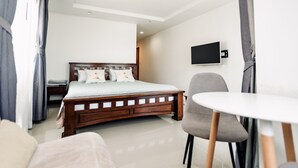 Ein modernes Hotelzimmer mit einem hölzernen Bett, einem kleinen runden Tisch, einem grauen Sessel und einem flachbildfernseher an der Wand.