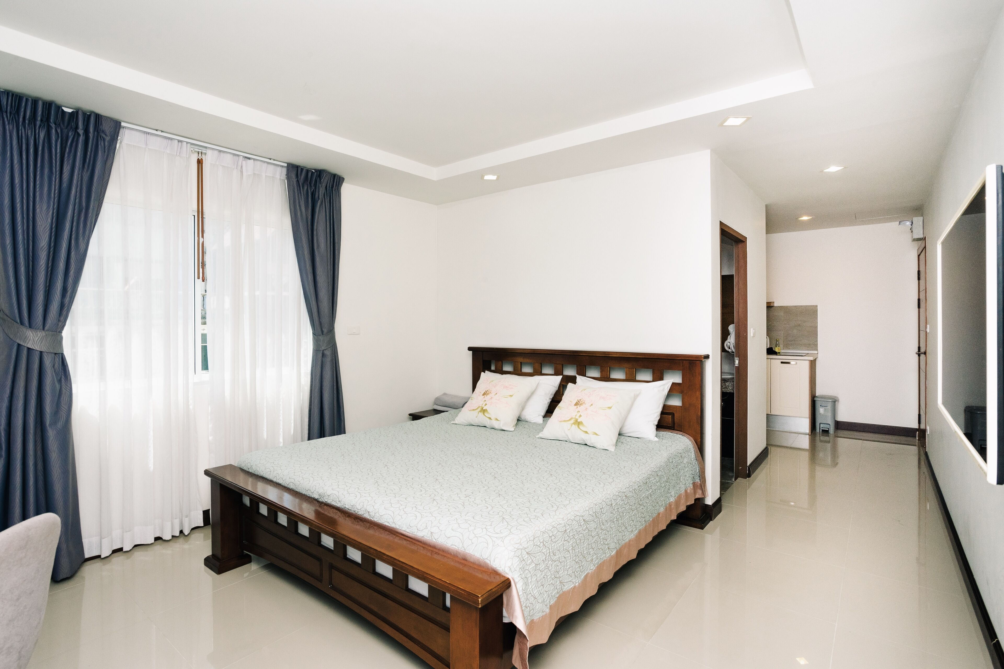 A modern bedroom with a wooden bed, a nightstand, and a large window with curtains.