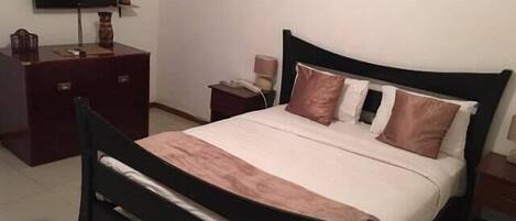 Un dormitorio ordenado con cama, escritorio, silla, televisor montado en la pared y un cuadro enmarcado sobre la cama.