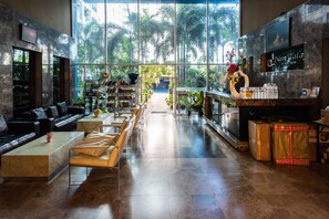A spacious lobby with a modern design, featuring a seating area with sofas and chairs, a reception desk, and large windows offering a view of the outdoors. - Nam Talay Condo by GrandisVillas (Pattaya)