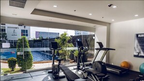 A gym with exercise equipment, a bench, dumbbells, and a view of a swimming pool and greenery outside.