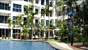 A swimming pool surrounded by palm trees and a white building with multiple windows.