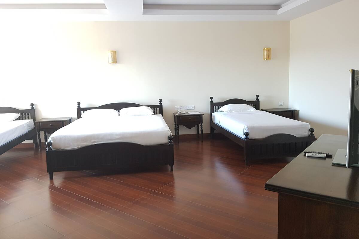 Quarto de hotel com duas camas de solteiro, piso de madeira, escrivaninha e televisão.