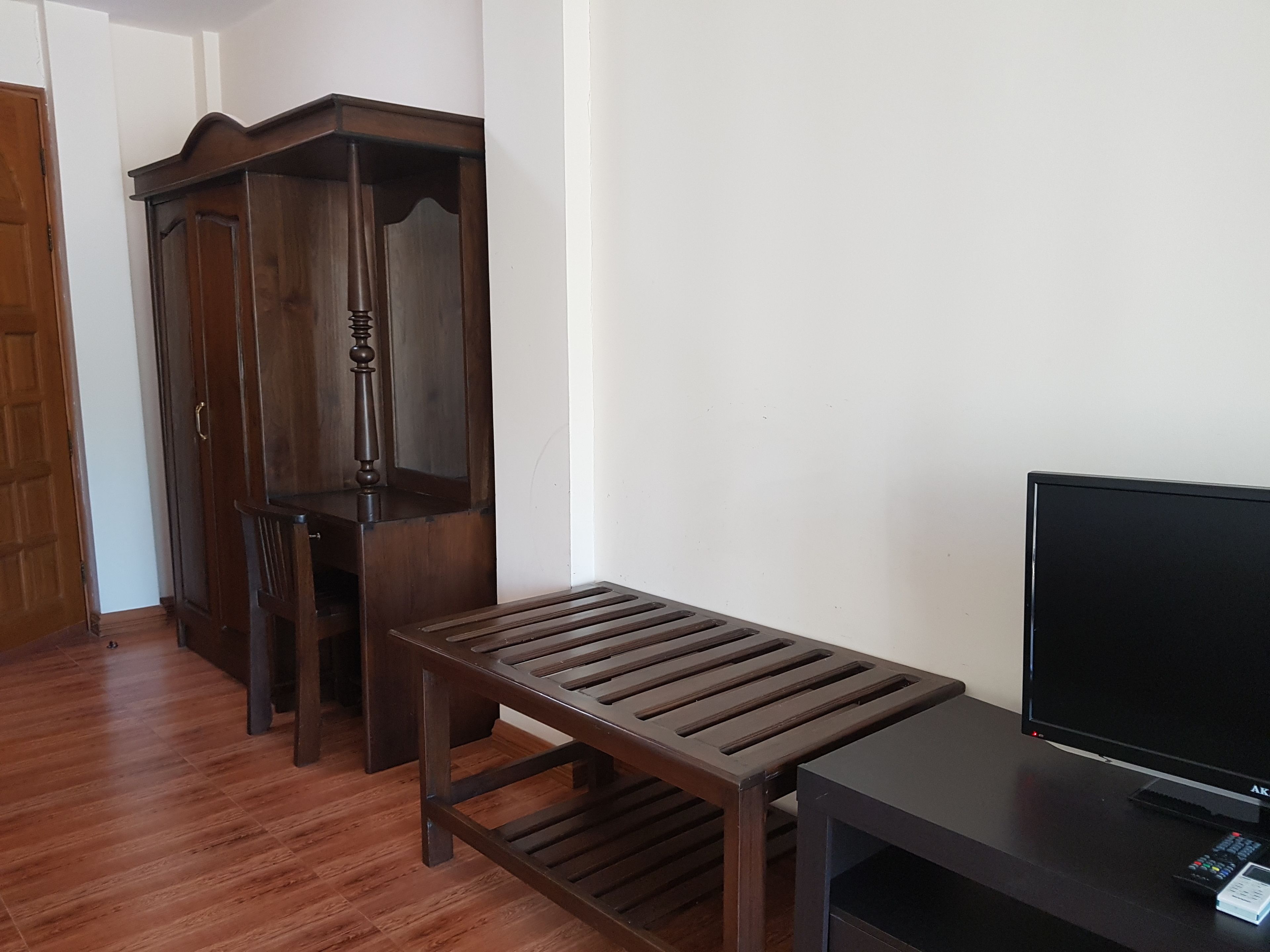 A room with a wooden bench, a TV stand, and a wooden wardrobe.