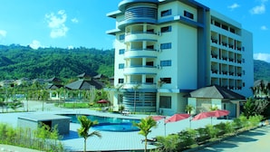 Un hotel de varios pisos con zona de piscina, rodeado de exuberante vegetación y colinas.