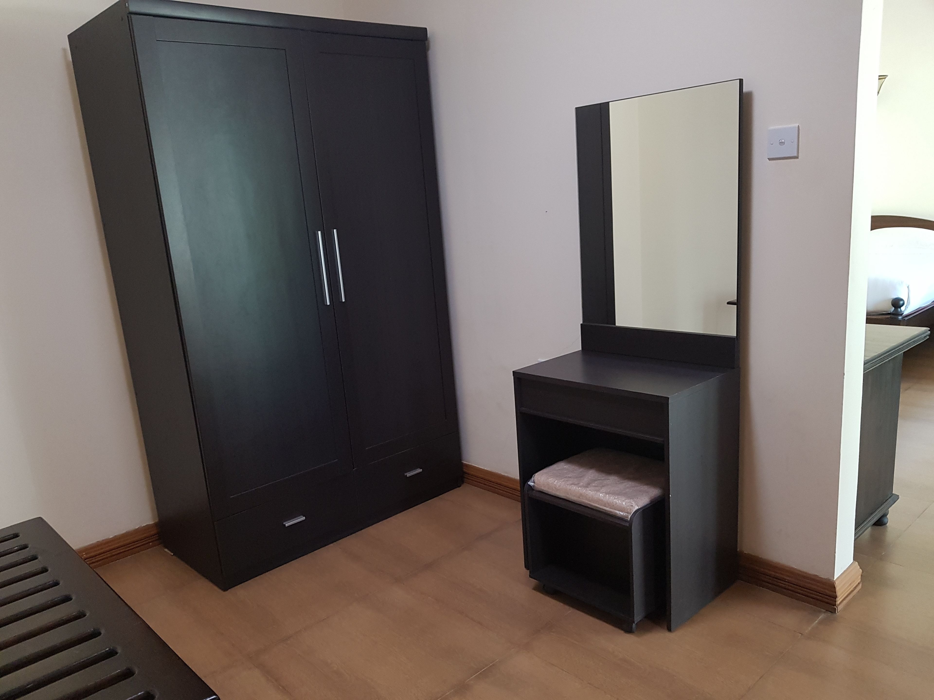 Een kamer met een grote kledingkast, een kaptafel met spiegel en een klein bankje.