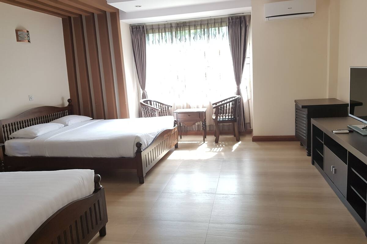 Quarto de hotel com duas camas de madeira, uma escrivaninha com televisão e uma cadeira.