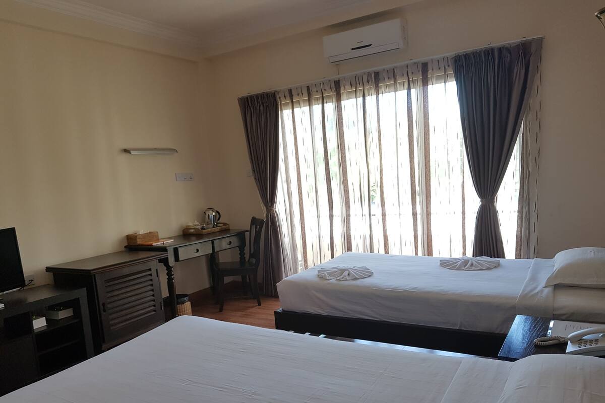 Quarto de hotel com duas camas, uma mesa com cadeira, televisão e aparelho de ar condicionado.
