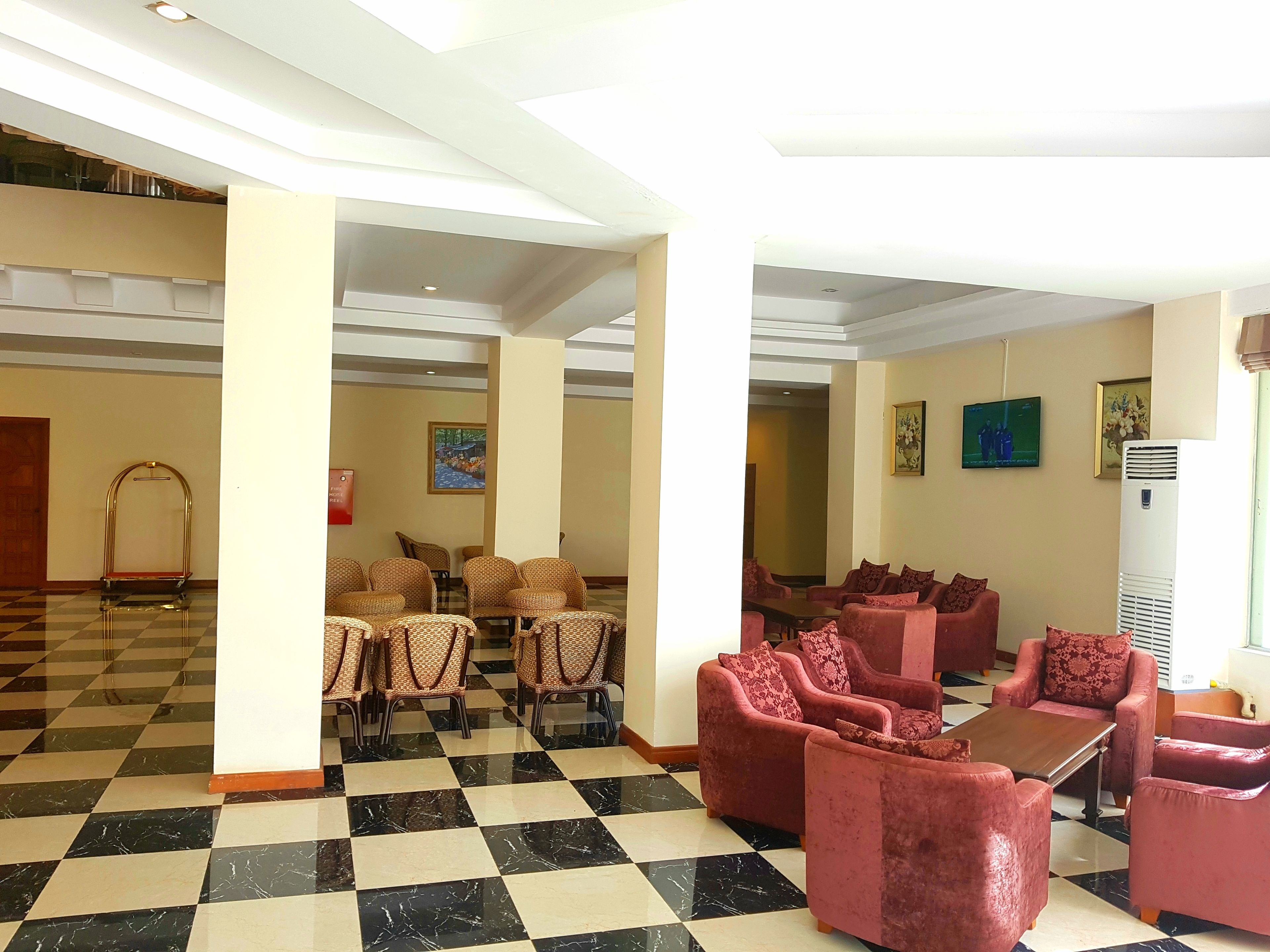 A lobby with checkered flooring, a seating area with cushioned chairs, a reception desk, and a large air conditioning unit.