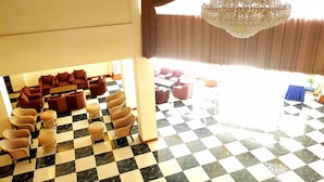 Un vestíbulo de hotel con suelo a cuadros, varias zonas de estar y una araña.