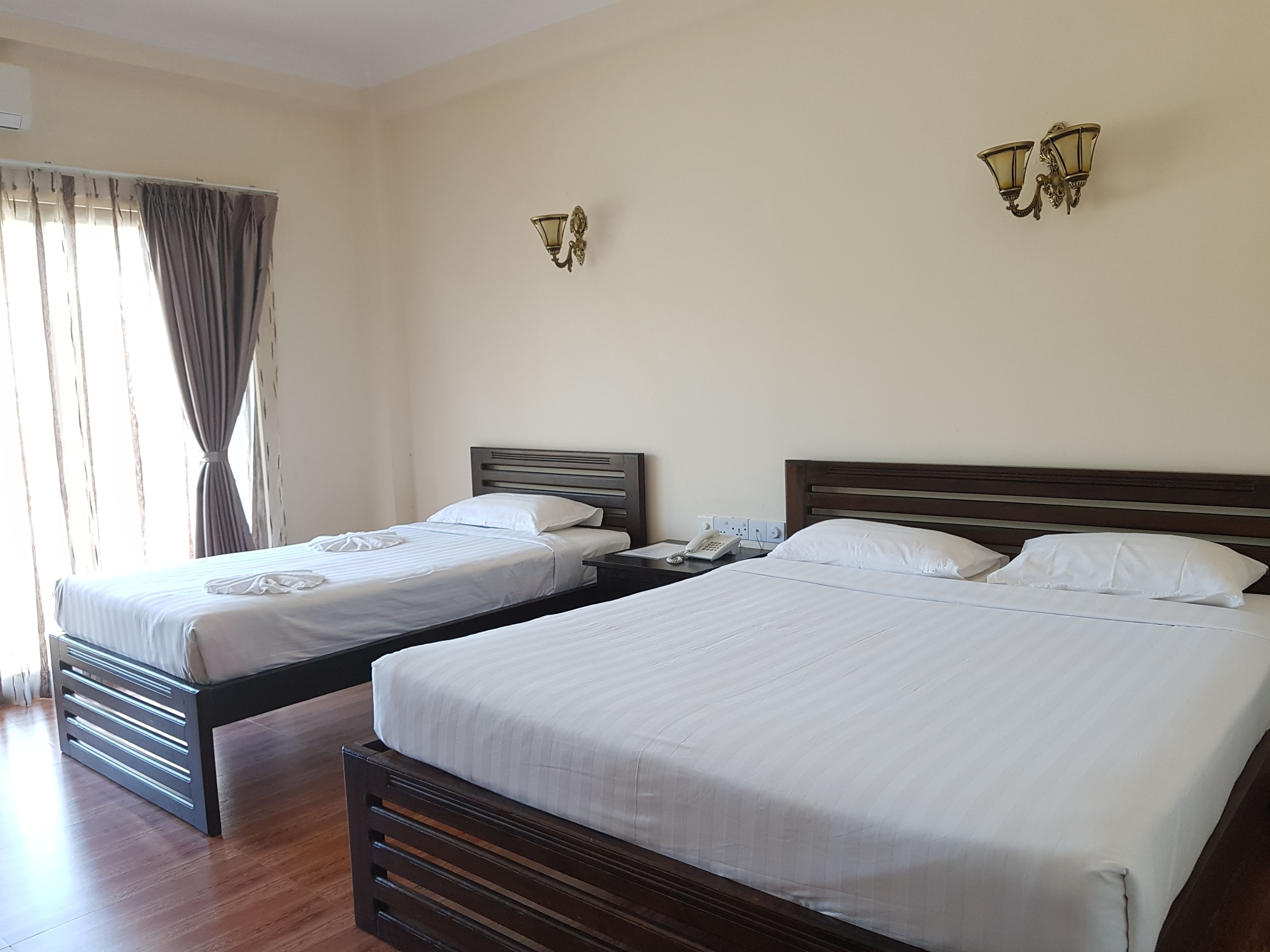 Two single beds with wooden frames and white bedding, a bedside table with a phone, and a wall-mounted light fixture.