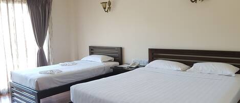 Two single beds with wooden frames and white bedding, a bedside table with a phone, and a wall-mounted light fixture.