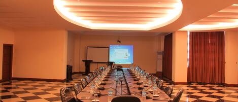 Un salón de conferencias con una larga mesa, sillas, una pantalla de proyector y un suelo a cuadros.