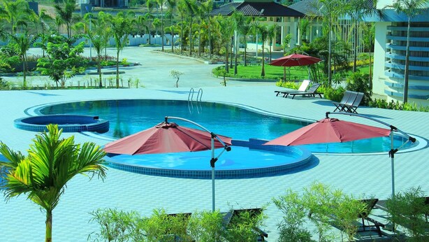 Un área de piscina en un complejo turístico, con varias piscinas, sillas de descanso y sombrillas.