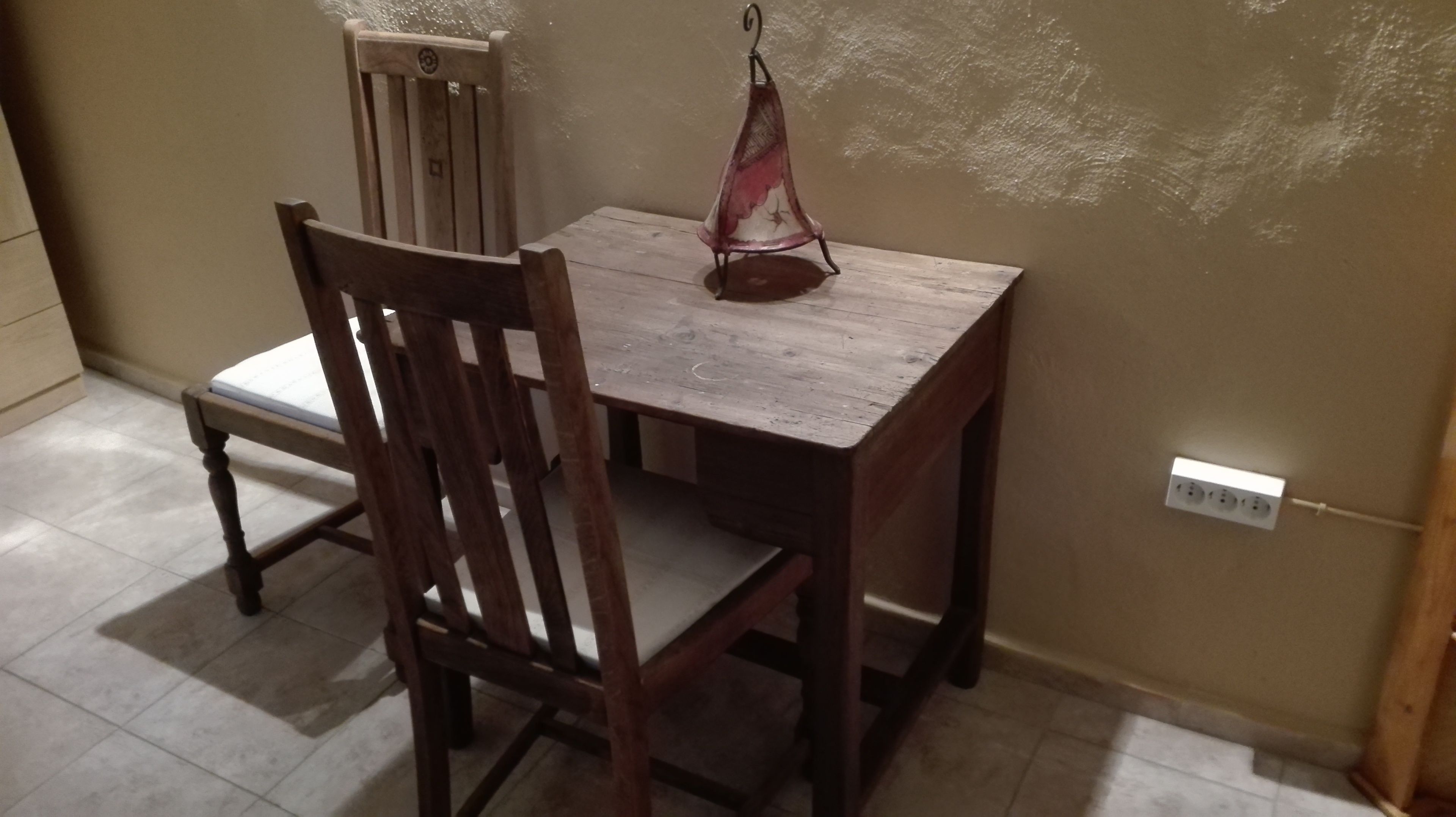 A wooden dining table with a chair, a hanging light fixture, and a power outlet on the wall.