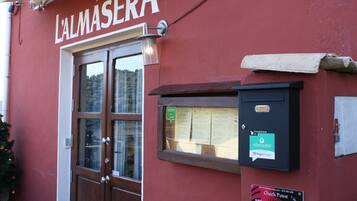 A red building with a wooden door and a sign that reads "L'ALMASERA".