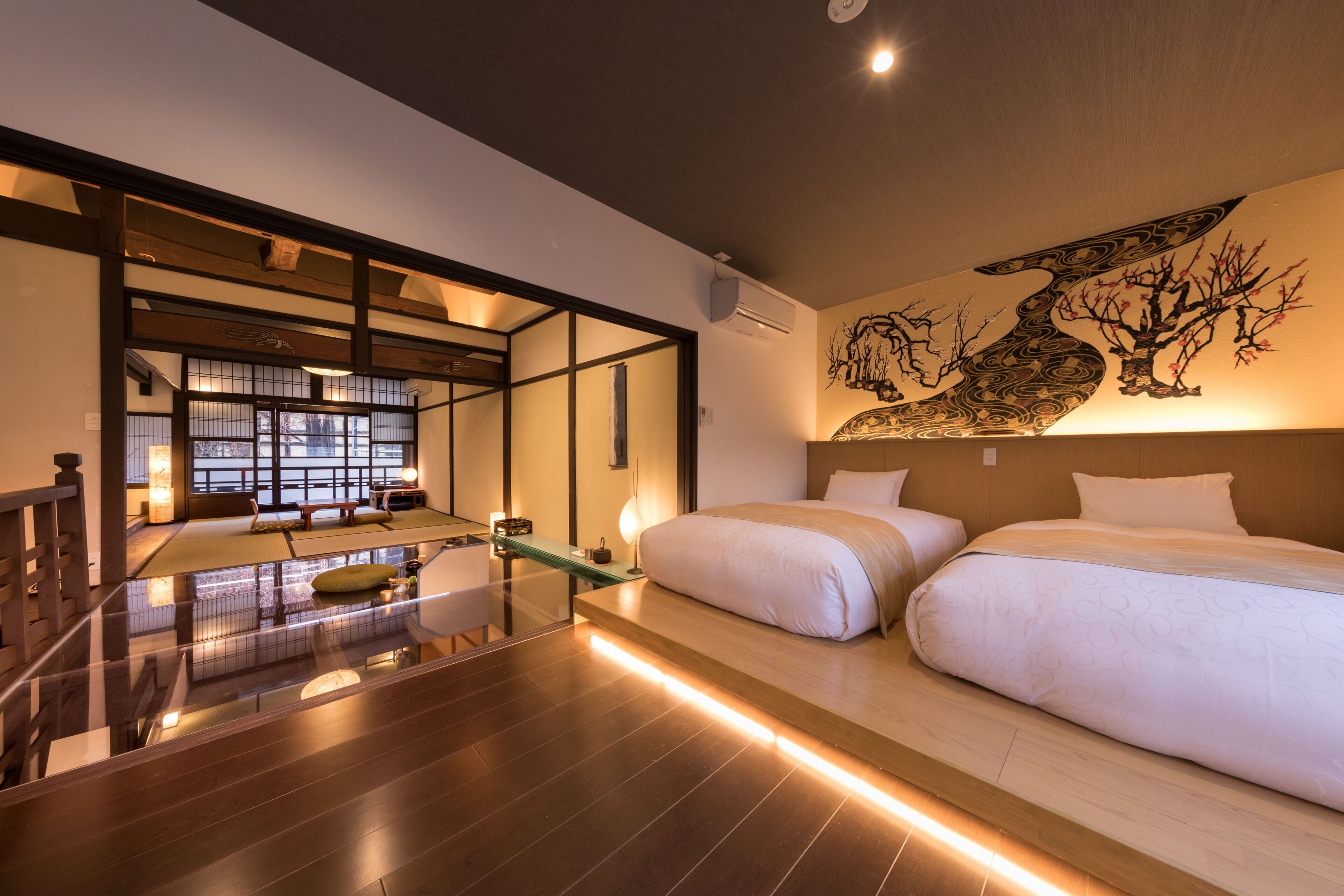 Una habitación de hotel moderna con una cama grande, un separador de vidrio y una habitación tradicional japonesa con suelo de tatami.
