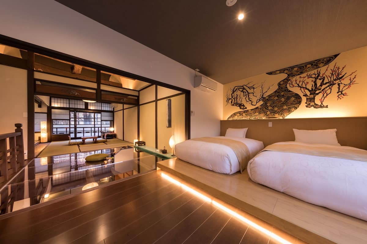 Ein modernes Hotelzimmer mit einem großen Bett, einer Glaseinteilung und einem traditionell japanischen Raum mit Tatami-Boden.