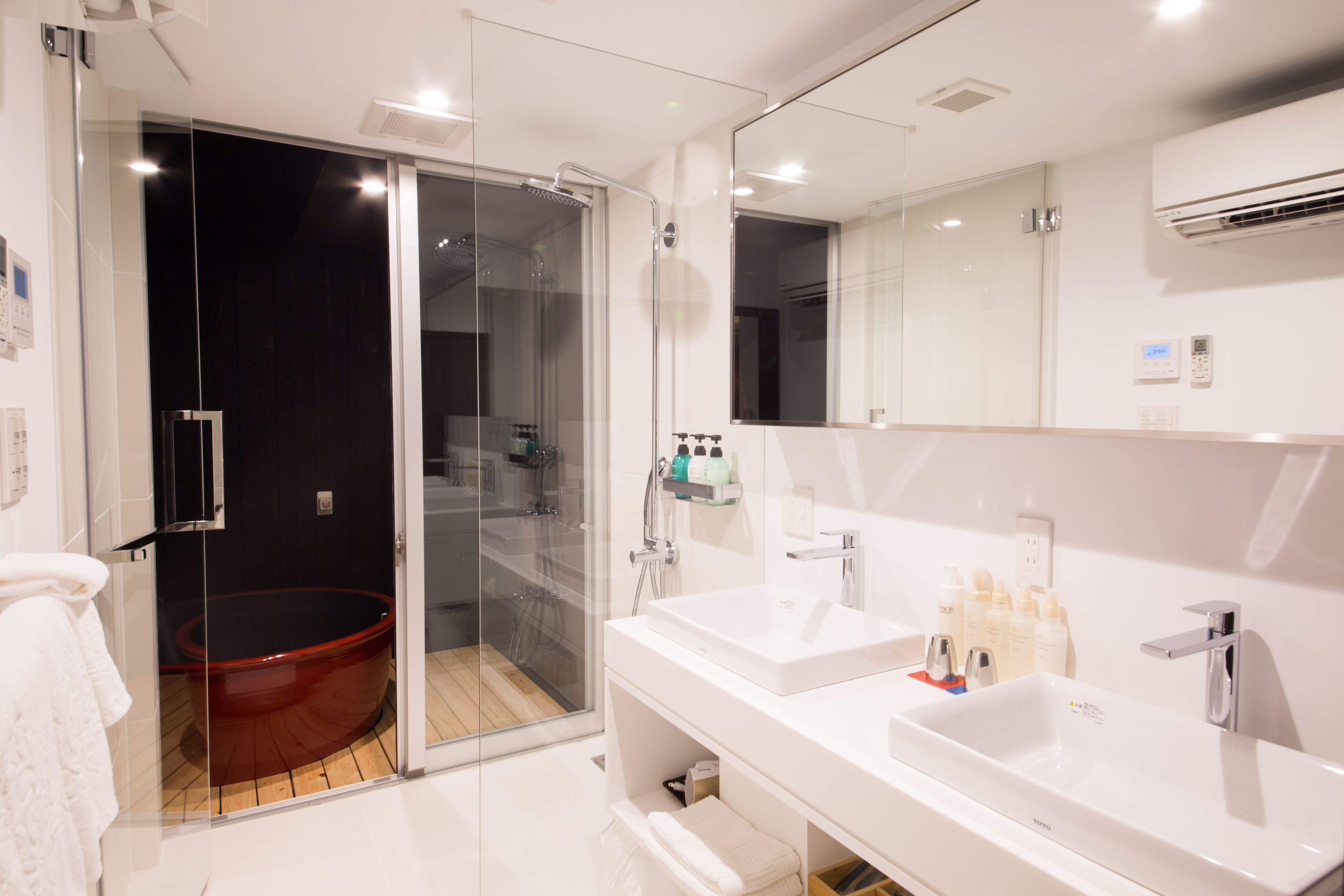 Un baño moderno con ducha de vidrio, dos lavamanos y un espejo grande.