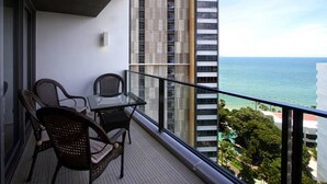 A balcony with two wicker chairs and a glass table, overlooking a cityscape and the ocean. - NorthPoint Pattaya Luxury Apartments by GrandisVillas (Pattaya)