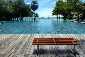 A wooden deck with a bench overlooking a pool area with clear blue water and trees. - NorthPoint Pattaya Luxury Apartments by GrandisVillas (Pattaya)