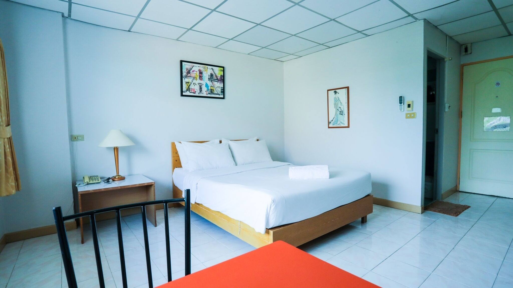 A hotel room with a bed, a nightstand with a lamp, a chair, and a door.