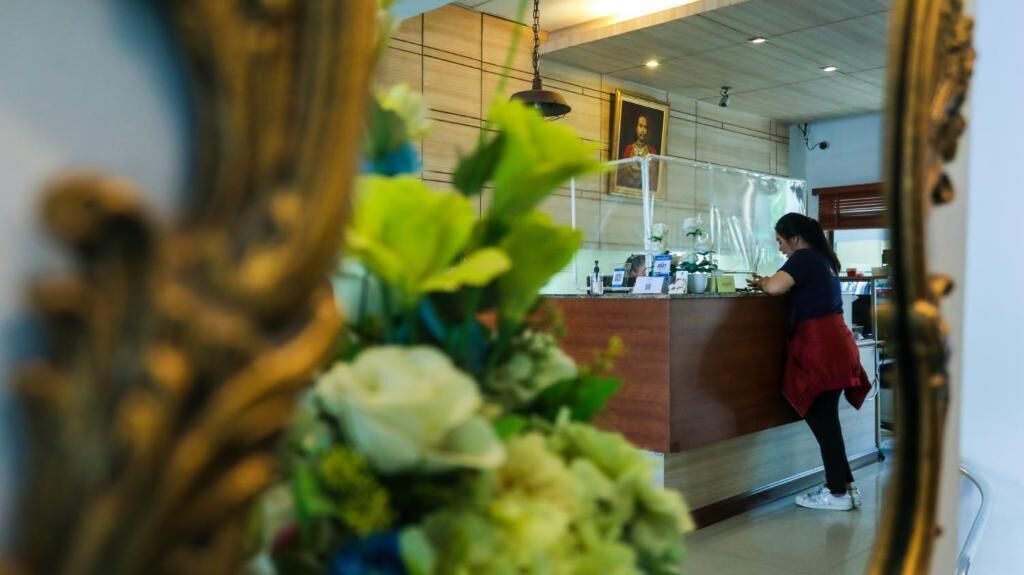 Un área de recepción con mostrador, un retrato enmarcado en la pared y una mujer de pie detrás del mostrador.