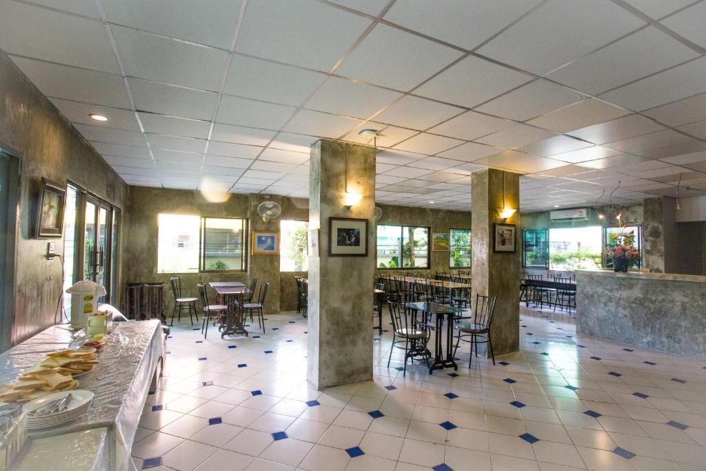 A spacious indoor area with tiled flooring, multiple tables and chairs, and large windows allowing natural light.