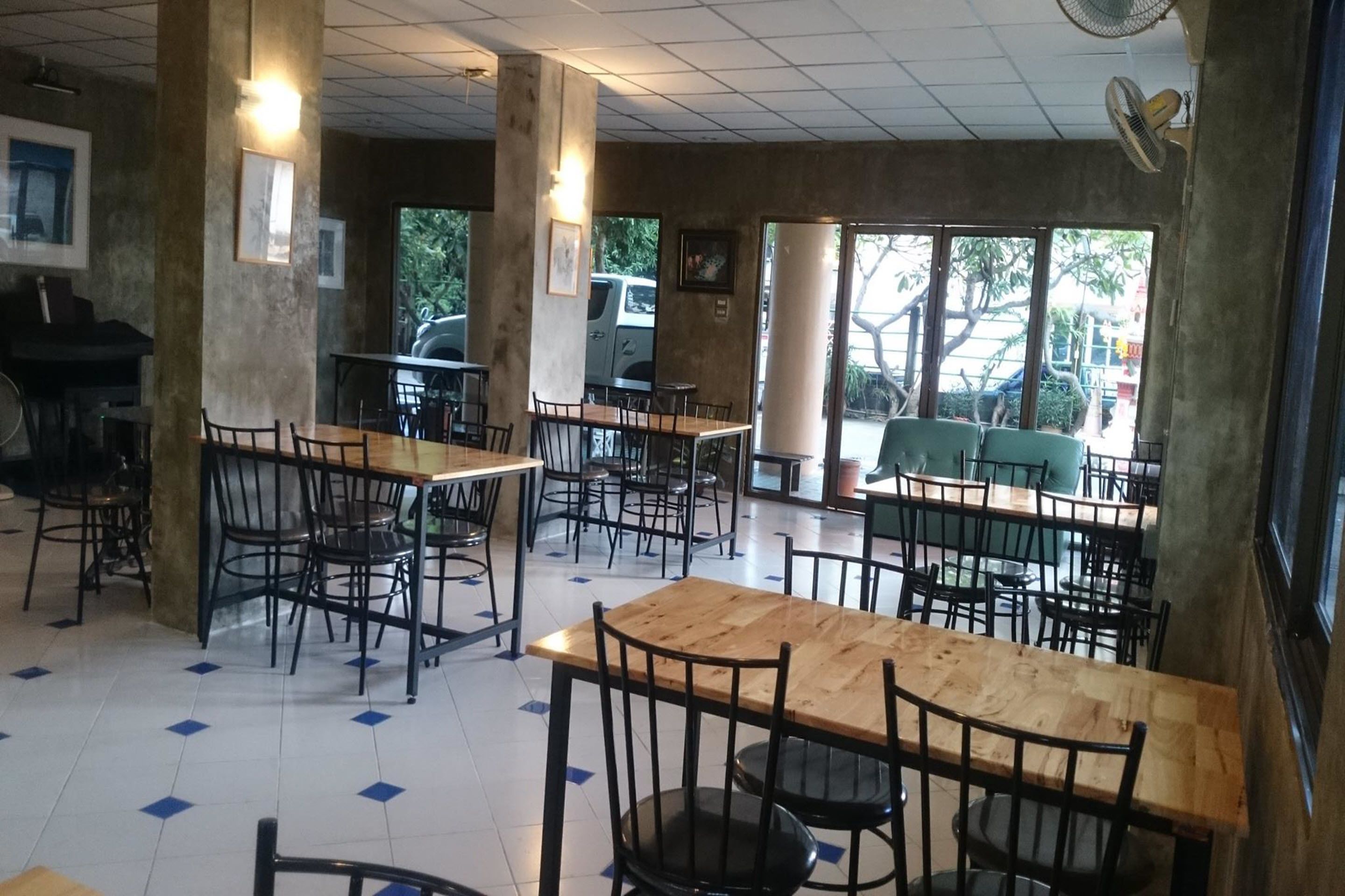 Un café avec de nombreuses tables en bois et des chaises noires, de grandes fenêtres et un piano dans un coin.
