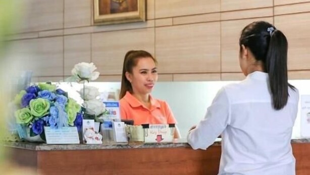 A reception desk with a framed portrait above it, a hanging light fixture, and a floral arrangement on the counter. - Central Place Hotel (Rayong)